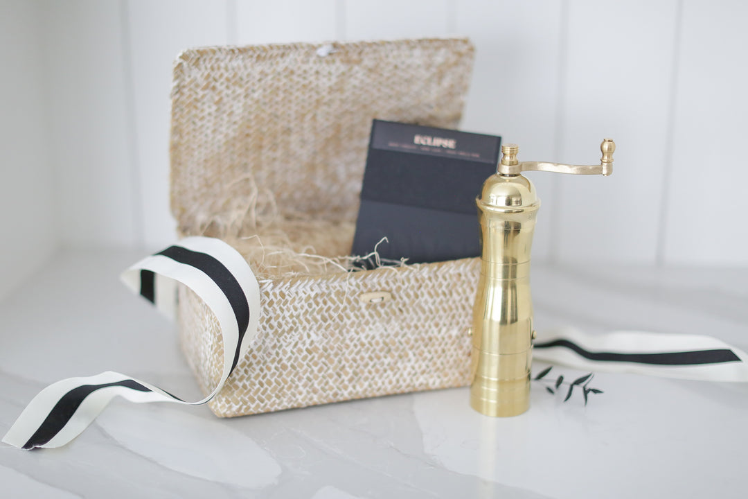 A gold coffee grinder in front of a decorative box with white and black ribbon.