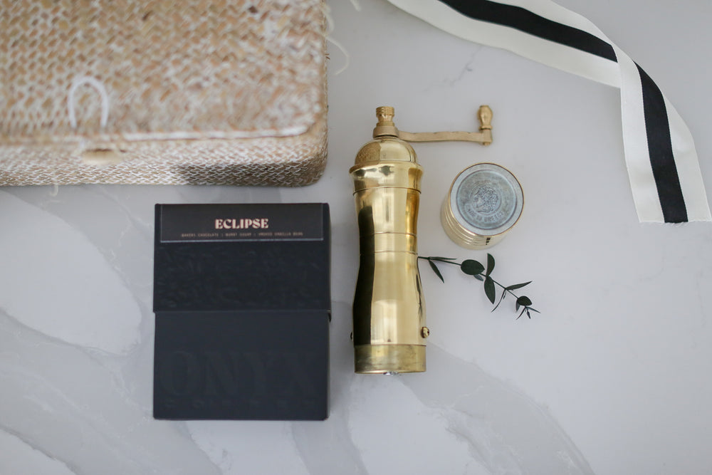 A gold coffee grinder on a marble counter next to an eclipse box with other decorative things around it.