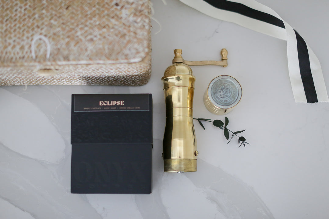 A gold coffee grinder on a marble counter next to an eclipse box with other decorative things around it.