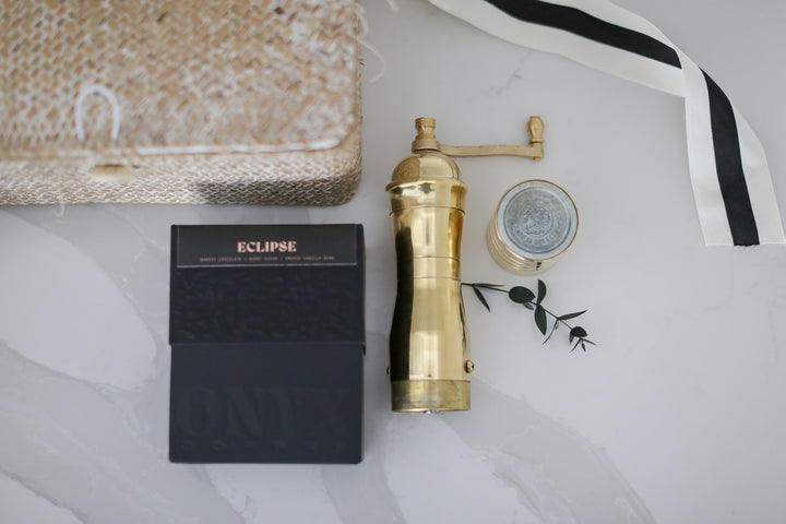 A gold coffee grinder on a marble counter next to an eclipse box with other decorative things around it.