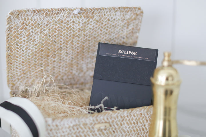 A black box containing gold words talking about a coffee mix. A gold coffee grinder in front of it. The box is inside of a decretive box.