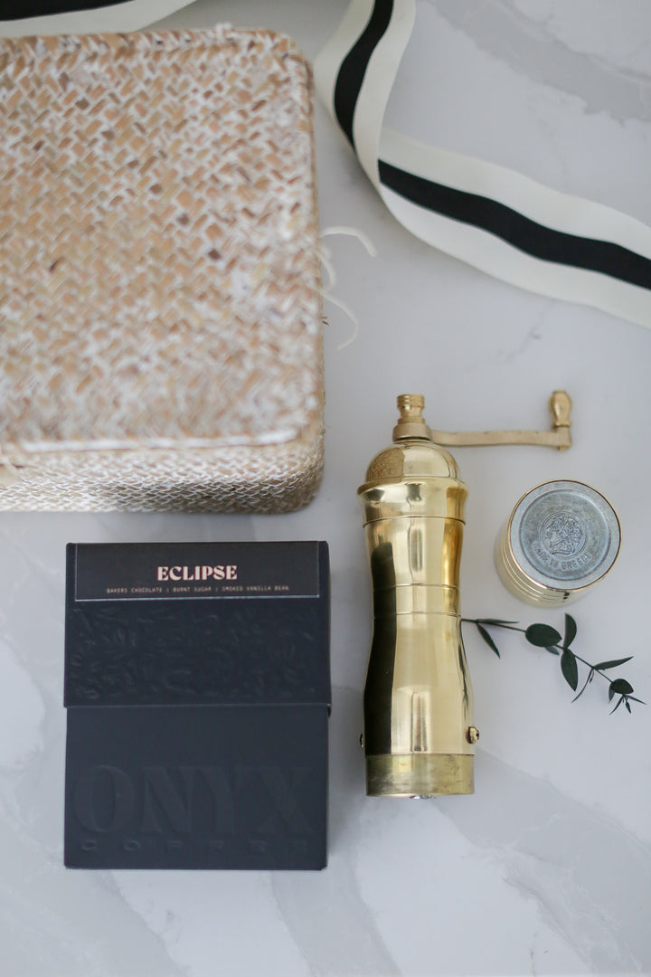 A gold coffee grinder and black box with a coffee mix on a marble counter with other decretive items around it.