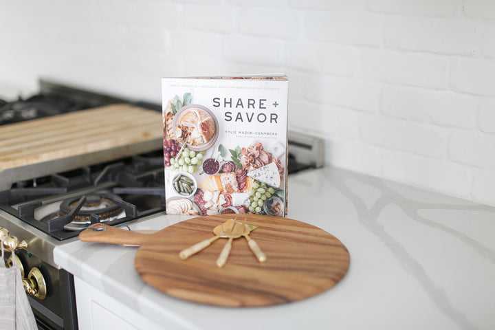 Wood charcuterie board with personalization available, Appetizer and charcuterie cookbook, idea book for charcuterie board, brass and rattan wrapped cheese utensils, white countertop, Mercy Forest Co., custom gifting for realtors, on-demand ready-to-ship gifts, packaged gift box, share and savor cookbook