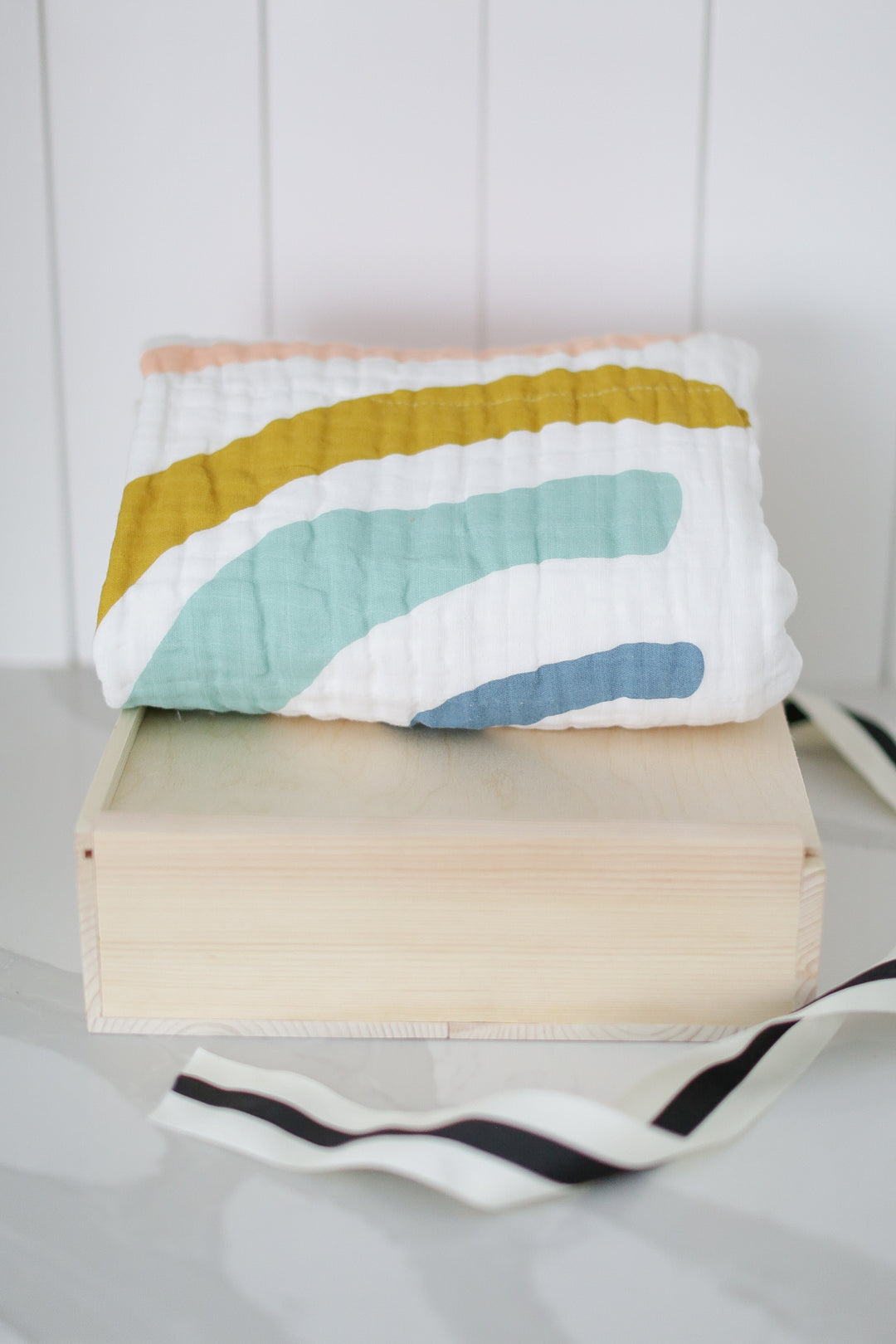 A wooden box with a decorative cloth on top, partially covered by a striped fabric, resting on a white surface.