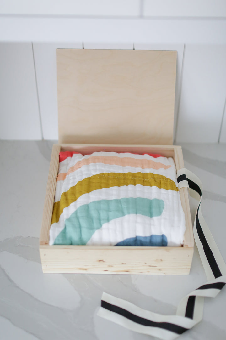 A wooden box with a decorative cloth on top, partially covered by a striped fabric, resting on a white surface.