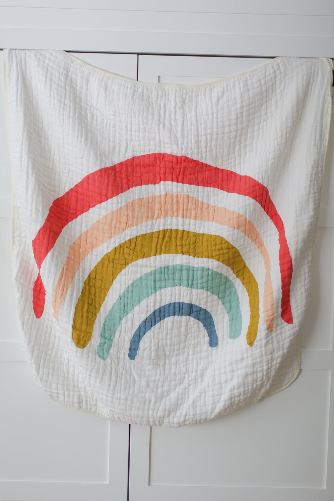 A white baby blanket with a rainbow on it, on a white surface.
