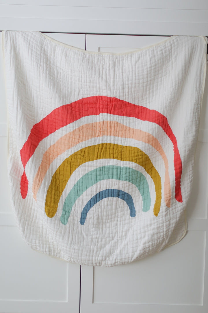 A white baby blanket with a rainbow on it, on a white surface.