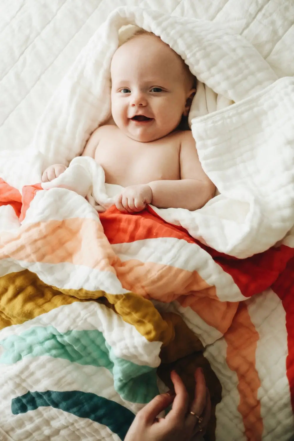 A baby wrapped in a white blanket with a rainbow on it.