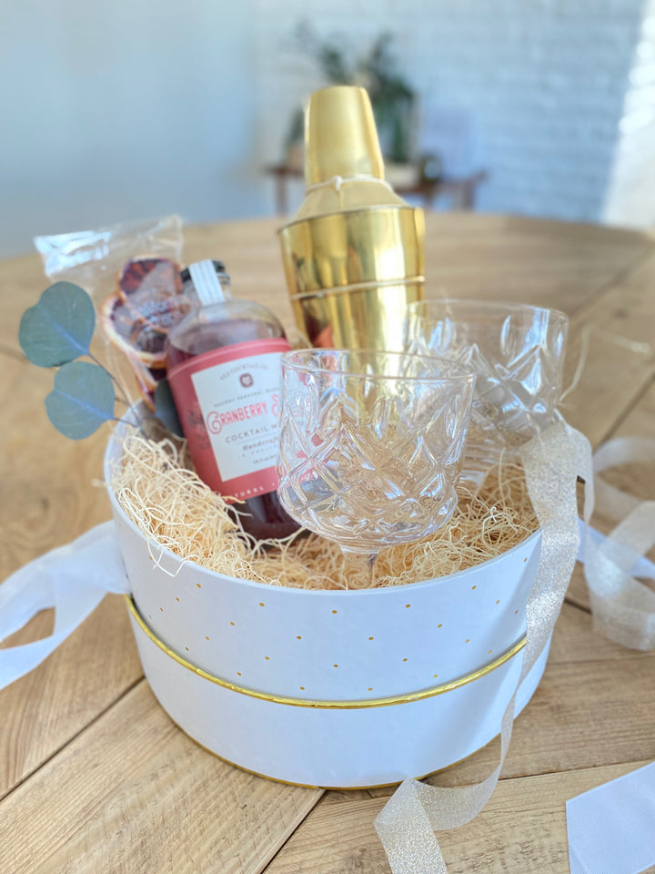 Cranberry spice drink mixer with brass cocktail shaker and faceted stemmed glass coupe cups. Mercy Forest Co. drink themed gift box, ready to ship. 