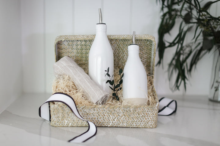 2 white oil cruet's in a giftbox with a grey and white striped tea towel.