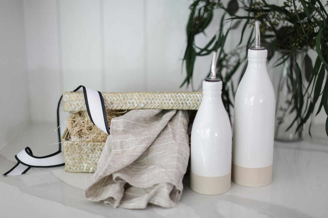 2 white oil cruet's in a giftbox with a grey and white striped tea towel.