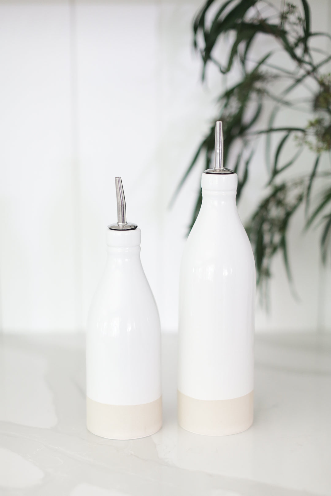 2 white oil cruet's on a white countertop with a white shiplap bachground.