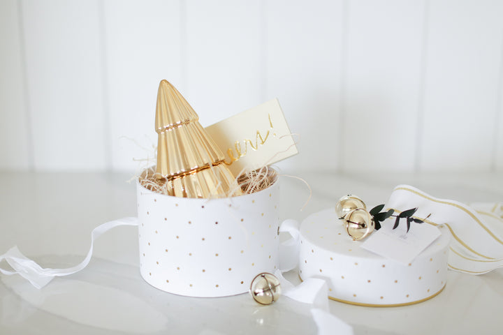 White round box with gold polka dots. excelsior with gold tree shaped candle and set of Cheers matches. Gold bells. Gifting made easy with Mercy Forest Co. 