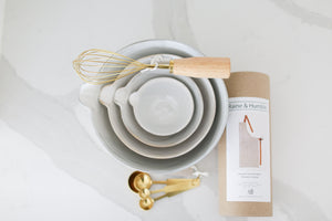 Custom curated gift box for people who like to bake, Custom curated gift box with baking bowls and utensils,  stoneware stacking baking bowls, brass wire whisk, brass measuring spoons, striped apron, Mercy Forest Co., real estate gifting, client gifting ideas, white kitchen countertops
