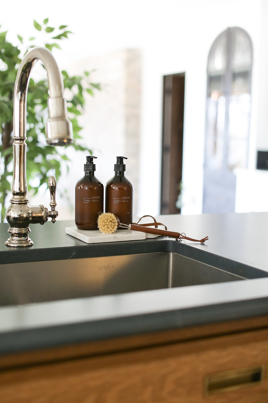 A beautifully presented gift box tied with a sleek leather ribbon. Inside, a stunning solid marble serving board with a unique fleur design takes center stage. Pampering hand soap and hand cream from Raine & Humble add a touch of luxury. A practical and stylish pot scrubber with a handle completes the set.